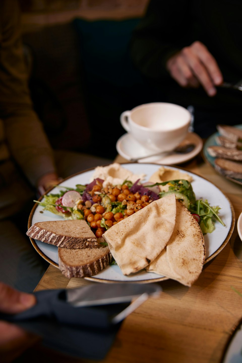 Piatto di insalata mediterranea con hummus e pane su un tavolo di legno.